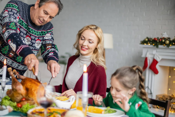 senior man cutting delicious roasted turkey during christmas dinner with happy family - Photo, Image
