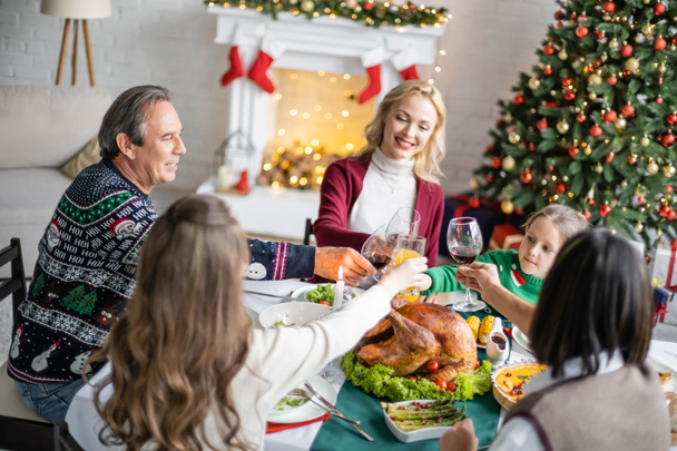cheerful interracial family clinking glasses near delicious roasted turkey on christmas dinner at home - Zdjęcie, obraz