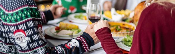 partial view of senior father and adult daughter holding hands and praying near blurred thanksgiving dinner, banner - Fotografie, Obrázek