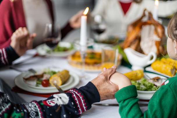 gedeeltelijk uitzicht op familie hand in hand tijdens het bidden voor dankzegging diner op wazig achtergrond - Foto, afbeelding