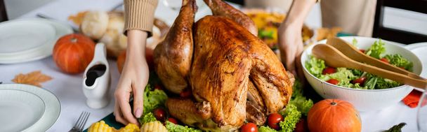 感謝祭のディナーのための新鮮な野菜サラダの近くでロースト七面鳥を提供する女性のクロップドビュー,バナー - 写真・画像
