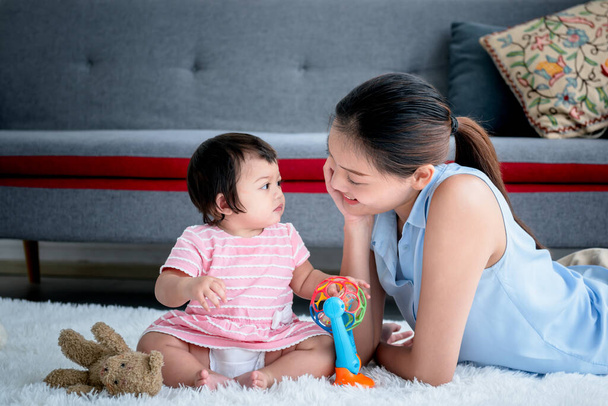 Asyalı anne ve 7 aylık kızı yerde oturup birbirlerinin gözlerinin içine bakıyorlar, aile ve bebek şirinliği kavramında ilişki kurmak için.. - Fotoğraf, Görsel
