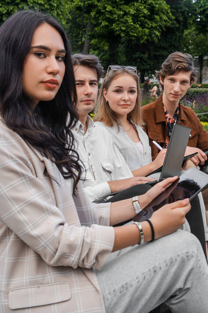 Shot van studenten zittend op bank in de buurt van fontein browsen laptop en tablet. - Foto, afbeelding