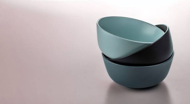 Three ceramic bowls of different colors in a stack. Isolated on a pale pink background. - Fotó, kép
