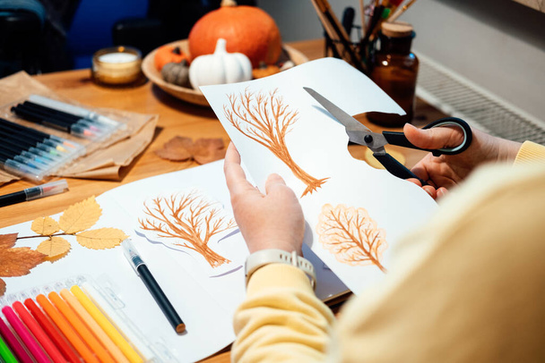 Осеннее ремесло для взрослых. Безликий портрет женщины, рисующей осенние деревья с маркерами и вырезающей коллаж из бумаги - Фото, изображение