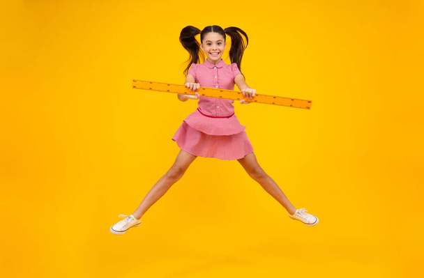 Teenager school girl study math or geometry lesson, measure the size. Mathematics ruler for measuring. Crazy jump, jumping kids. Happy positive and smiling schoolgirl - Фото, изображение