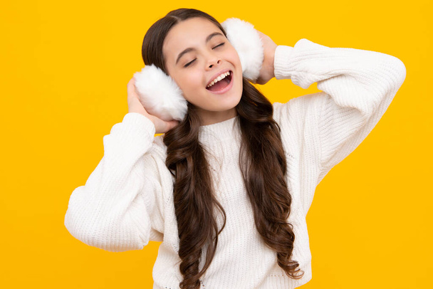 Teenager girl with winter warm earmuff ear-flaps over isolated yellow background. Winter christmas holidays, new year mood. Kids warm clothes - Foto, afbeelding