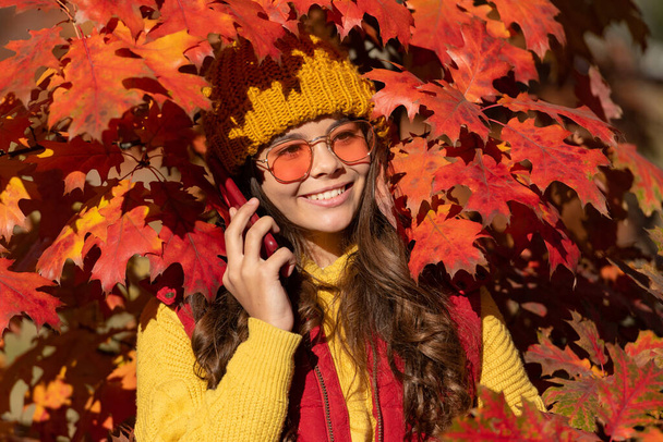 Child girl in autumn fall park outdoor, kids fun face. happy teen kid in sunglasses talking on phone at autumn leaves on natural background. - Photo, Image