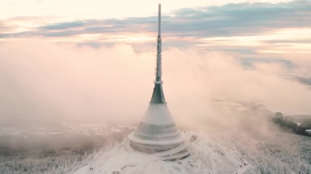 La densa niebla rodea la torre Jested con una gran aguja en el día de invierno. Arquitectura moderna en lo alto de la montaña forestal en República Checa vista aérea - Metraje, vídeo