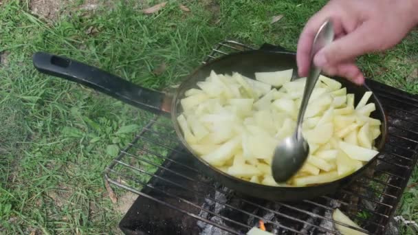  a szakács keze megkeveri a krumplit egy kanállal egy serpenyőben a grillen, a fűben. - Felvétel, videó