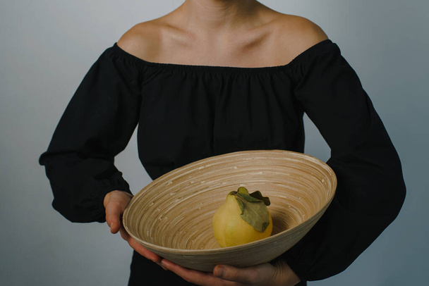 молодая женщина с бамбуковой тарелкой и спелой айвой внутри. Высокое качество фото - Фото, изображение