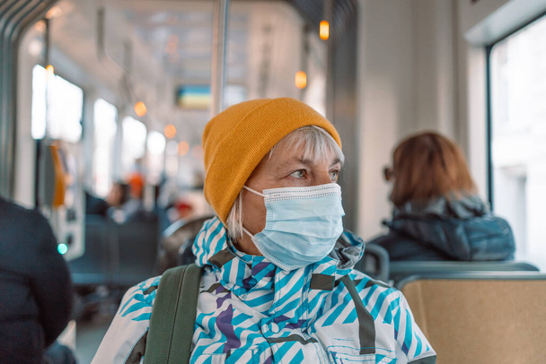 Starsza Europejka nosząca maskę na twarzy siedząca w pociągu COVID-19 epidemia koronawirusa.  - Zdjęcie, obraz