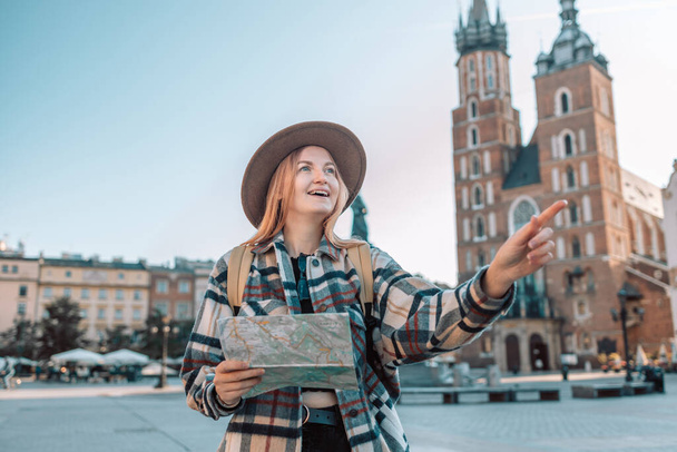 Fröhliche Wanderin mit trendigem Blick auf der Landkarte bei Auslandsreisen im Herbst, fröhliche Touristin auf der Suche nach einem Hotel auf einem Atlas in einer fremden Stadt im Urlaub.  - Foto, Bild