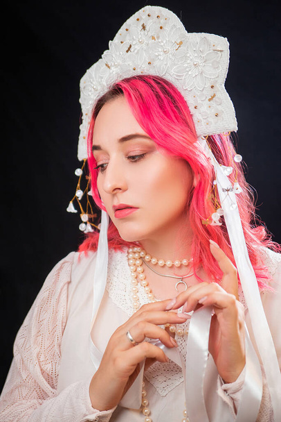 Close-up portrait of a woman with pink hair in a white dress with a kokoshnik on her head posing isolated on a black background. - Photo, Image