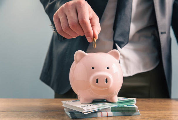 Man putting money into piggy bank. Savings concep - Фото, изображение