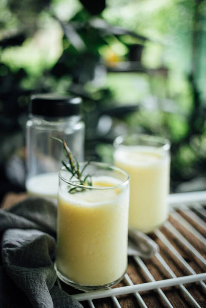 Χυμός καλαμποκιού smoothie σε λευκό ράφι τοποθετείται στο ξύλο και το φυτό φόντο στο σπίτι γλάστρες κήπο. κάθετη φωτογραφία - Φωτογραφία, εικόνα