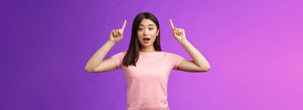 pobudzony słodkie zaskoczony Azji dziewczyna w różowy t-shirt mówi o niesamowite wiadomości wskazując podniesione palce w górę, wskazać top reklamy, otwarte usta zdumiony, podekscytowany stoisko niebieski tło. - Zdjęcie, obraz