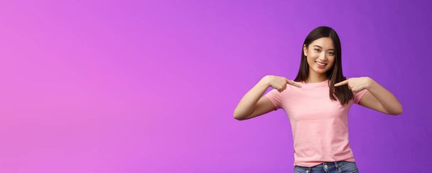 Aktiivinen energinen ystävällinen hellä aasialainen tyylikäs tyttö esittelee itsensä, osoittaa rintaa ylpeänä, hymyilee ylpeänä, kuvailee omia saavutuksia, kehuskelee saavutuksia, seisoo tyytyväinen violettiin taustaan. - Valokuva, kuva