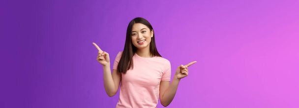 Charismatic relaxed cute asian woman short haircut pointing sideways introduce variety choices, showing left and right products, smiling joyfully, easily making decision, stand purple background. - Foto, afbeelding