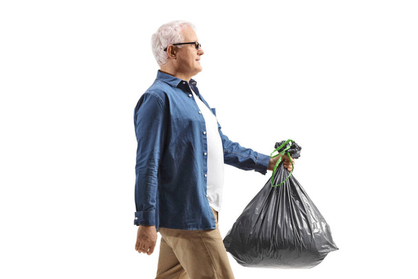 Profile shot of a mature man walking and carrying a plastic waste bag isolated on white background - Photo, Image