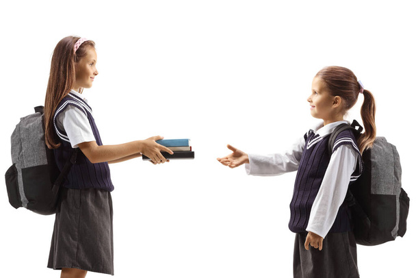 Older girl giving books to a younger schoolgirl isolated on white background - Фото, изображение
