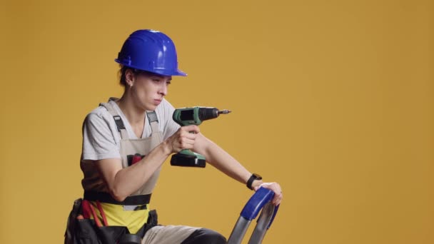 Confident constructor using electric power drill to screw nails, working with engineering machine on construction refurbishment. Woman drilling with nail gun to repair, over yellow background. - Footage, Video
