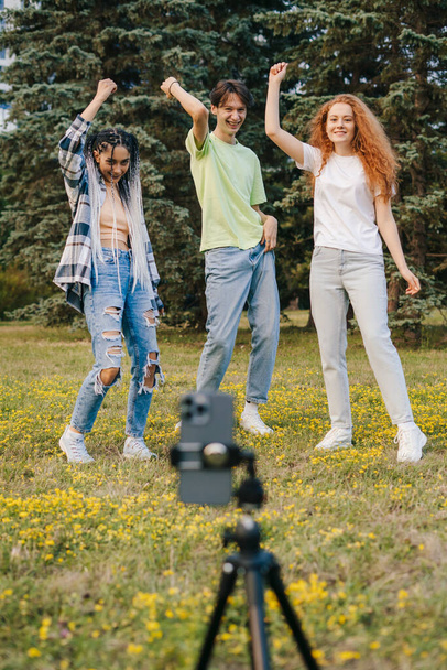 Gli adolescenti stanno girando un video di danza con un telefono nel parco estivo. Sfida sui social media. Il concetto di ballerino, influencer, artista dei social media. - Foto, immagini