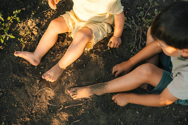 Vista de cerca de algunos pies de niños sentados en el suelo, sucios. Hermoso retrato de niños verdes jugando tierra. - Foto, imagen