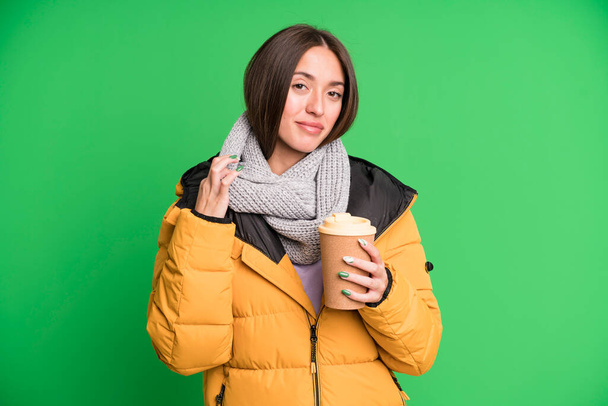 young pretty woman looking arrogant, successful, positive and proud wearing a coat and holding a take away coffee - Photo, Image