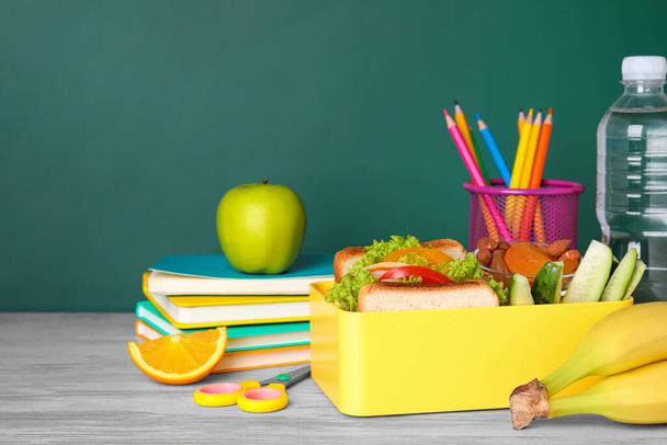 Lunch box with healthy food and different stationery on wooden table near green chalkboard, space for text - Фото, изображение