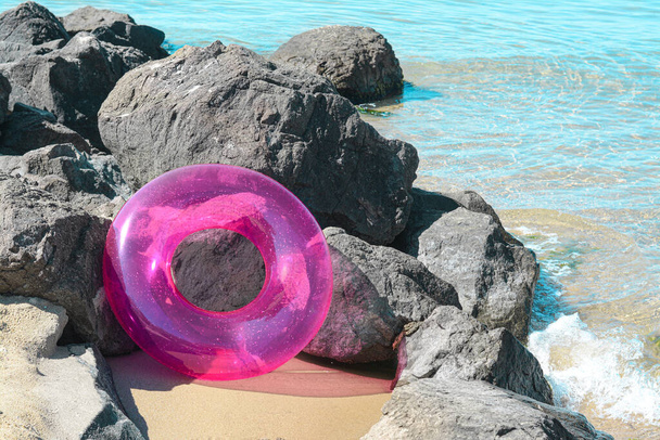 Bright inflatable ring on sandy beach near rocks - Фото, зображення
