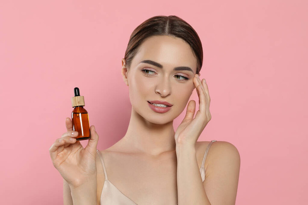 Young woman with bottle of essential oil on pink background - Foto, Imagem
