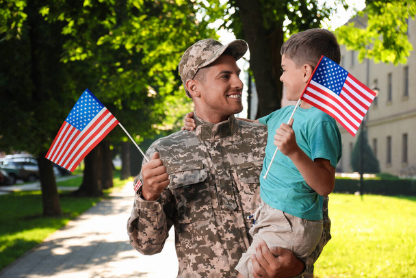 Солдат и его маленький сын с американскими флагами на улице. День ветеранов в США - Фото, изображение