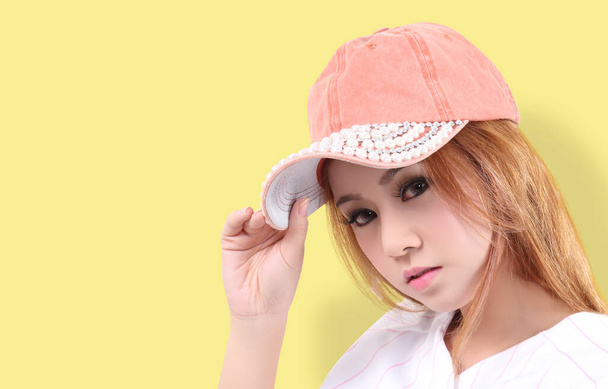jonge aziatische vrouw dragen sport cap levensstijl en gele achtergrond in studio - Foto, afbeelding