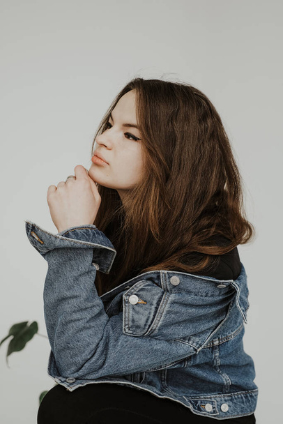 Portrait of a girl holding her head in denim jacket. Studio portraits of a girl with variety of facial expressions and poses. - Photo, image