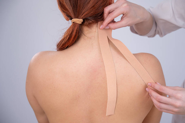Female doctor glues kinesio tapes on the patients shoulder - Foto, Imagem