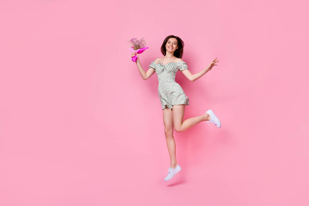 Full length photo of cheerful funny girl dressed off shoulders outfit jumping holding flowers empty space isolated pink color background. - Foto, Imagen