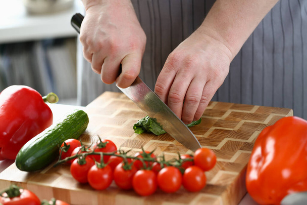 Chef is preparing salad of spinach cucumbers and tomatoes in kitchen. Closeup of chef hands cutting vegetables with knife on cutting board - Foto, immagini