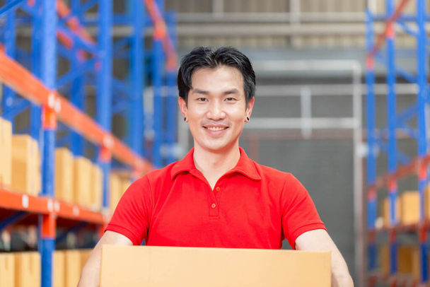 El hombre sostiene la caja de cartón que camina a través en almacén al por menor, trabajador de almacén que trabaja en almacén de fábrica - Foto, Imagen