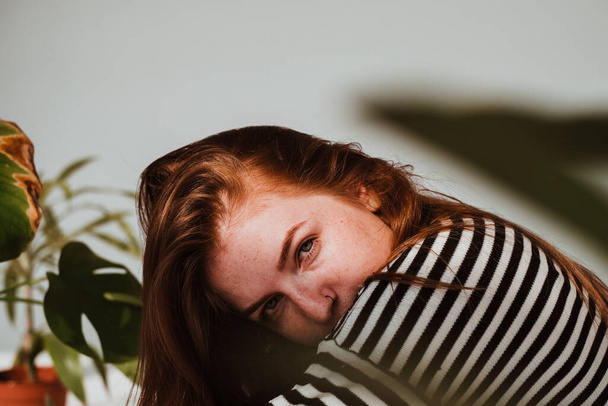 Close-up van mooi meisje met rood haar en groene ogen op zoek naar camera met serieuze look met planten in de buurt. Studio portretten van rood haar meisje met verschillende emoties en stijlen. - Foto, afbeelding