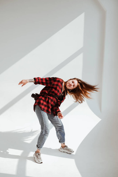 Rouge hair girl dancing in plaid red shirt and jeans with camera on her back. Studio portraits of red hair girl with variety of emotions and styles. - Photo, Image