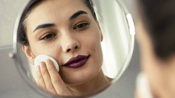 Отражение в зеркале красивой женщины, делающей косметический уход за кожей - Фото, изображение