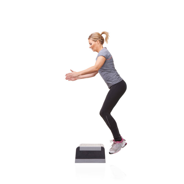 Vyskakuje ve snaze o kondici. Usmívající se mladá žena dělá aerobik na aerobní krok proti bílému pozadí - Fotografie, Obrázek