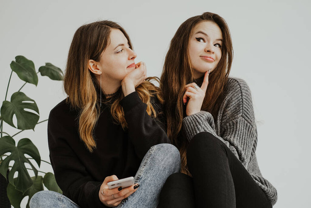 Στιγμιότυπο δύο νεαρών γυναικών να κοιτάζονται, να χαμογελούν και να κάνουν γκριμάτσες. Πορτραίτα δύο γυναικών που κάθονται η μία δίπλα στην άλλη με ένα φυτό τέρας κοντά, αγκαλιασμένοι, εκφράζοντας συναισθήματα και συναισθήματα. - Φωτογραφία, εικόνα