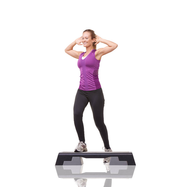 Taking steps to improve her fitness. A smiling young woman doing aerobics on an aerobic step against a white background - Photo, Image
