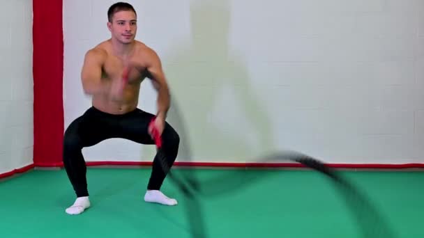 Pěkný záznam v reálném čase hezký svalnatý mladý muž pomocí bojových lan pro cvičení v tělocvičně. Zaměřuje se na provádění cvičení, motivační video, kopírovací prostor - Záběry, video
