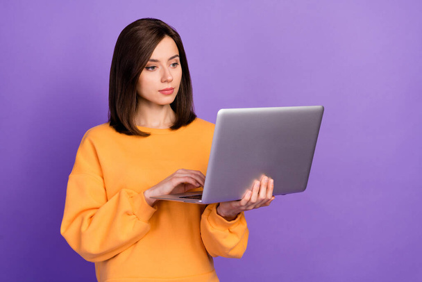 Photo of young adorable pretty girlish woman confident professional programmer wear yellow sweater hold computer typing isolated on purple color background. - Fotó, kép
