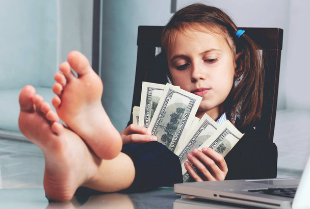 Zamknij humorystyczny portret szczęśliwy cute młoda dziewczyna biznesu liczy US Dollar pieniądze z gołymi stopami na stole.  - Zdjęcie, obraz