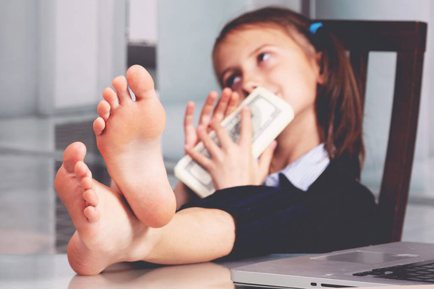 Portrait of very happy cute young business girl with bare feet on the table and counts money profit. Selective focus on feet - Photo, Image
