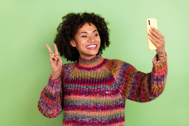 Photo of funky millennial curly hairdo lady show v-sign wear red sweater isolated on green color background. - Foto, Imagen